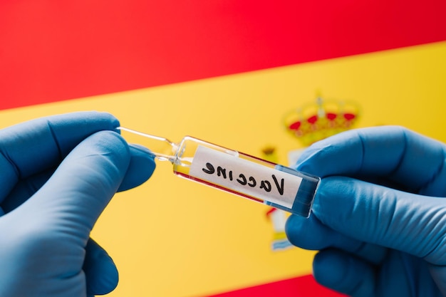 Fight against coronavirus Medical worker develops vaccine for Covid19 Hands in medical gloves with vaccine against Spain flag background Health care concept