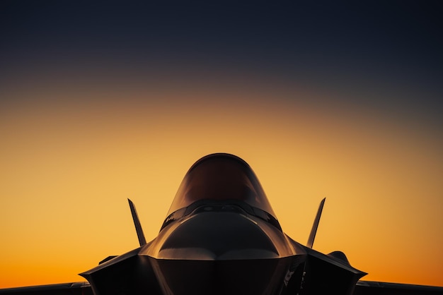 A fighter jet is silhouetted against a sunset sky.