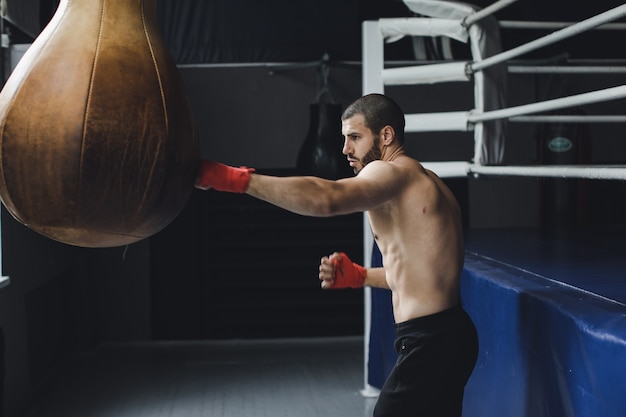 Боец тренирует некоторые удары ногами с боксерской грушей, ударяет боксерскую грушу на темном фоне, черная боксерская груша весит в тренажерном зале высококачественные кадры k