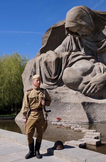 Боец Красной Армии в форме времен Второй мировой войны с пулеметом у исторического памятника на Мамаевом кургане в Волгограде