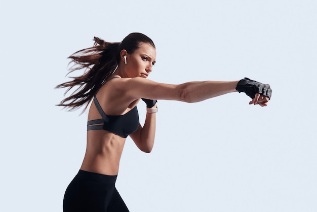 Fighting. Attractive young woman boxing while standing against grey background