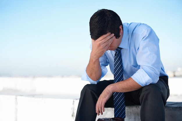 Photo fighting deppression an upset corporate man sitting on the rooftop of a building with his head in his hands