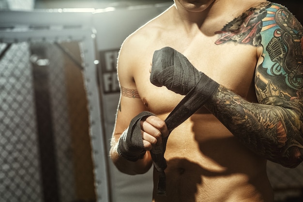 Fighting preparation. Cropped shot of a ripped tattooed fighter wrapping his hands