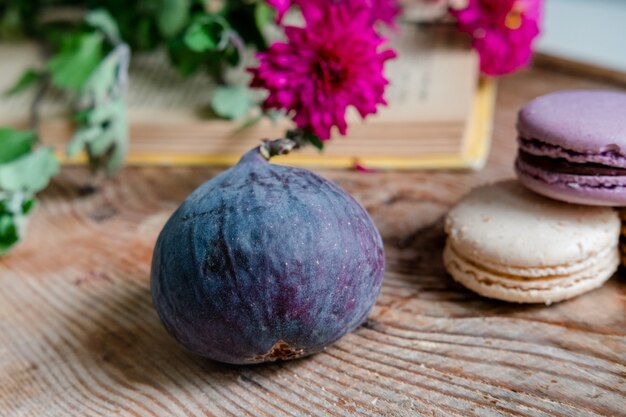 Fichi su uno sfondo di fiori rossi, macarons e libro su un tavolo di legno. telaio orizzontale. bella frutta su un tavolo di legno. mattina colazione francese. serve per un appuntamento