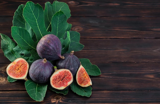 Figs and halves of several fruits on fig tree leaves on an old\
wooden table horizontal frame with copy space seasonal fruits fig\
harvest background or mediterranean diet articles