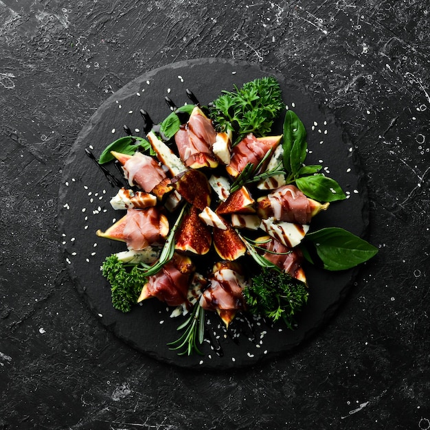 Figs with prosciutto and blue cheese and basil on a black stone plate Food Top view Free space for your text