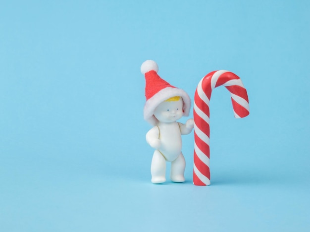 A figure of a baby in a red hat and a large Christmas candy on a blue background. Minimalism. The concept of the new year.