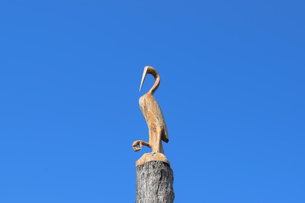 Figure of crane on the stump of a tree against the blue sky Figures of animals made of wood Woodcarving