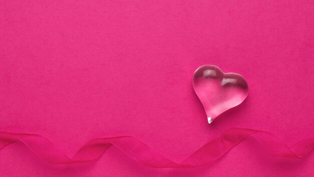 A figure of a glass heart and a ribbon on a pink background. The concept of Valentine's Day.