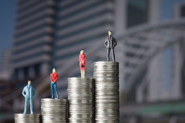 Рисунок миниатюрного бизнесмена, стоящего на стопке монет