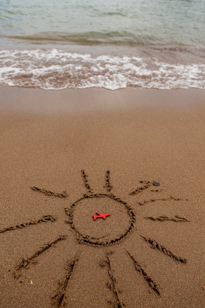 Рисунок красного самолета и нарисованное солнце на песке на берегу. отдых и туризм самолетом до моря. Изображение солнца и символ самолета у моря.