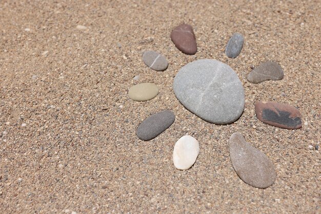 Figure of sun is made of stones on beach sand