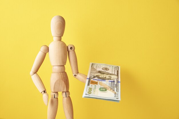 Figure of wooden holds cash money on yellow background