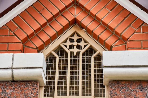 Figured lattice with decorations on window located under mezzanine roof brick part of cottage facade