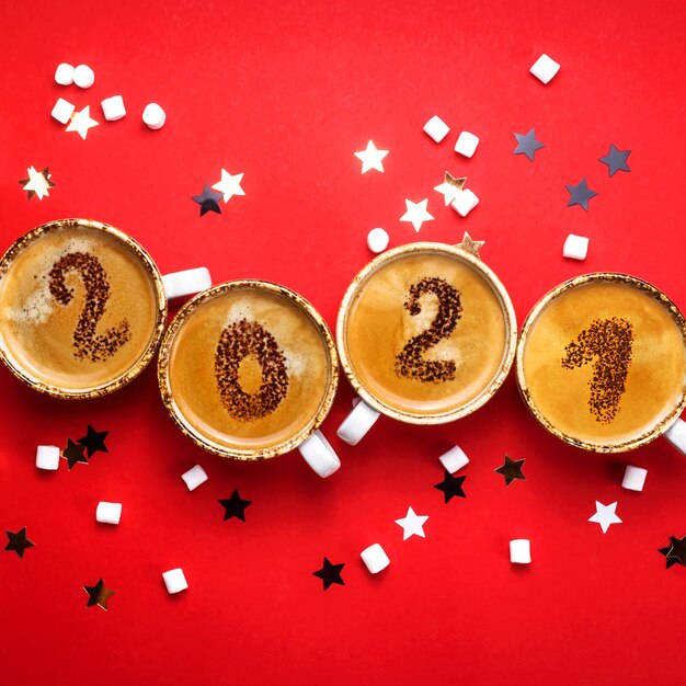 Figures 2021 as a symbol of the New Year on cups of hot aromatic coffee on a bright red