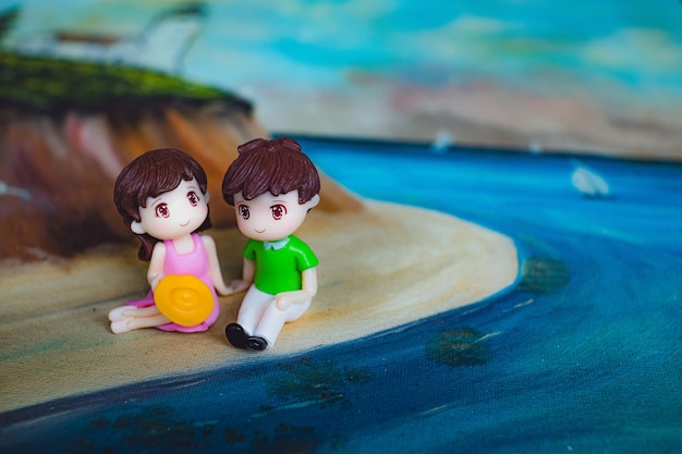 figures of couple holding hands while resting on artwork of sandy beach between sea and mountain