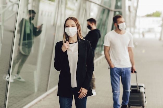 Figure di giovani in maschere protettive vicino all'aeroporto. viaggio sicuro durante una pandemia. concetto di viaggio in aereo, quarantena e pandemia