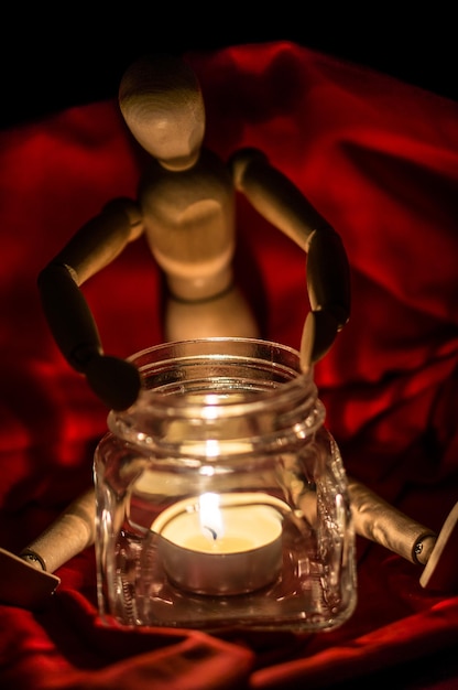 Figurine with burning tea light candle in glass jar on red fabric
