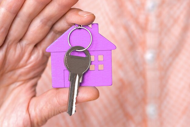 Figuur van een paars mini-huisje met de sleutels in de hand van een man op een beige achtergrond