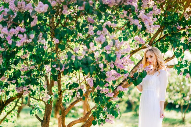 Fijn kunstportret van jong blondemeisje in witte elegante kleding in de zomer bloeiende lilac tuin.