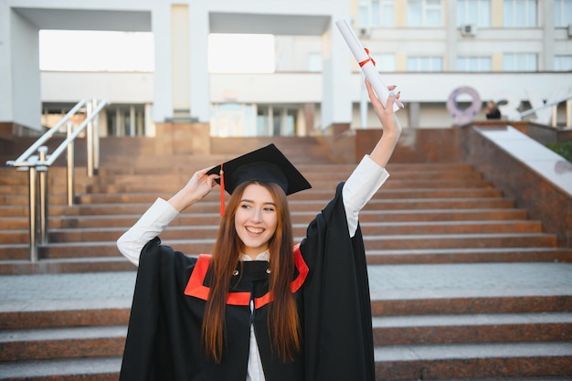 Fijne afstudeerdag voor een jonge vrouw, erg mooi met afstudeerpet, glimlach groot voor de camera terwijl ze haar diploma vasthoudt