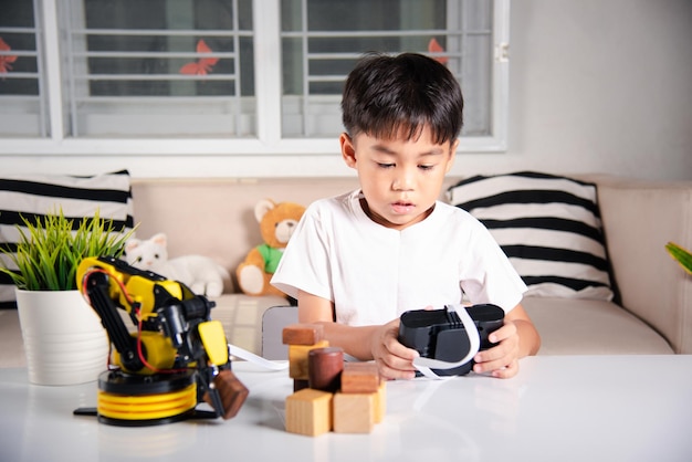 Fijne Aziatische kleine jongen die afstandsbediening gebruikt om robotarm te spelen voor het oppakken van houtblokken