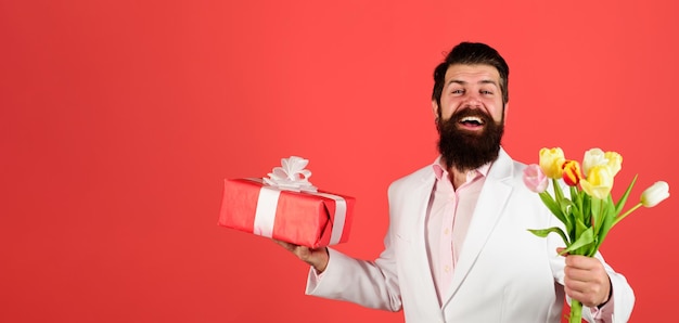 Fijne bebaarde man met geschenkdoos en boeket tulpen, lentebloemen en geschenkdoos, boeket van