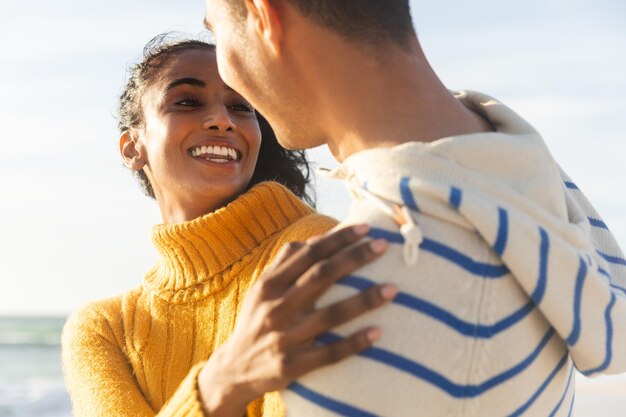 Foto fijne biraciale jonge vrouw die naar vriendje kijkt terwijl ze hem omhelst op het strand op zonnige dag. levensstijl, liefde en weekend.