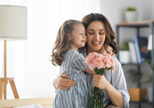 Fijne dag Kinddochter feliciteert moeder en geeft haar bloemen Moeder en meisje glimlachen en knuffelen Gezinsvakantie en saamhorigheid