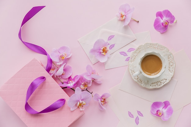 Fijne flatlay-compositie met 's ochtends kopje koffie met melk of cappuccino, letters, roze cadeauzakje en orchideebloemen op lichtroze oppervlak. Prachtig ontbijtconcept