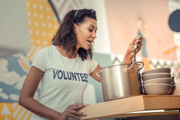 Foto fijne geur. vrolijke aardige vrouw die kippenbouillon klaarmaakt terwijl ze als vrijwilliger werkt