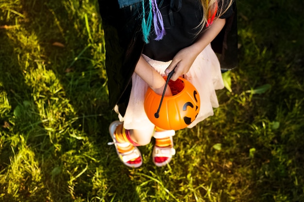 Fijne Halloween-dag Klein meisje gekleed in een heksenkostuum houdt emmer met snoep en toverstaf vast