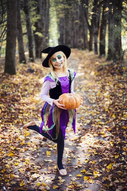 Foto fijne halloween. een grappig meisje in een heksenkostuum speelt met een pompoen aan de vooravond van halloween.