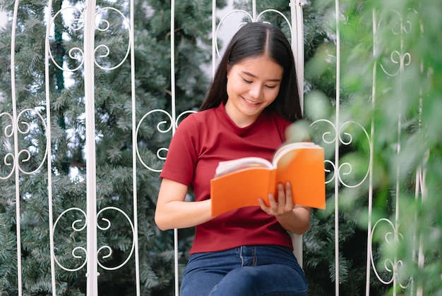 Fijne jonge mooie Aziatische vrouw ontspant op een gezellig balkon en leest met plezier een boek Lifestyle