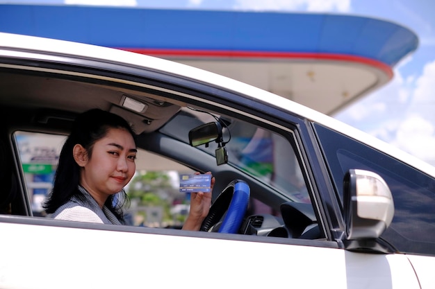 Fijne mooie Aziatische vrouw die in haar auto zit en creditcardbetaling toont bij een benzinestation