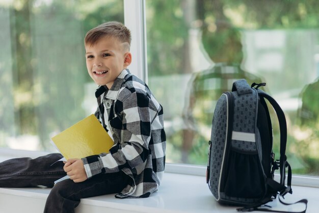 Fijne schooljongen in vrijetijdskleding met rugzakken die lacht en notities leest in notitieboekjes terwijl hij thuis huiswerk maakt