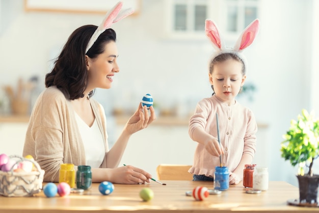 Fijne vakantie! Een moeder en haar dochter schilderen eieren. Familie voorbereiden op Pasen. Schattig klein kindmeisje draagt konijnenoren.