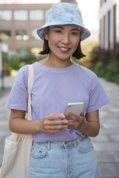 Fijne vrolijke aziatische vrouw die vrijetijdskleding draagt met een mobiele telefoon die naar de camera kijkt