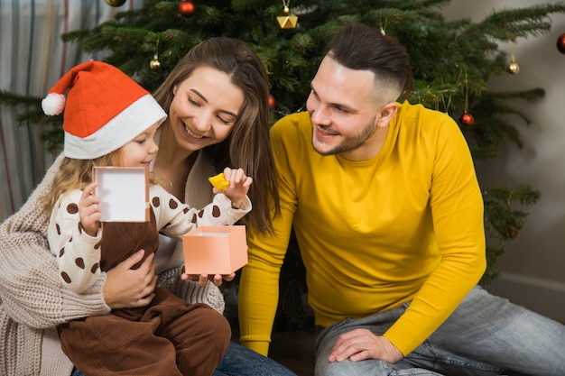 Fijne wintervakantie en prettige kerstdagen, vader, moeder en dochtertje wisselen geschenken uit in de buurt van dennenboom. Oudejaarsfamilie thuis.