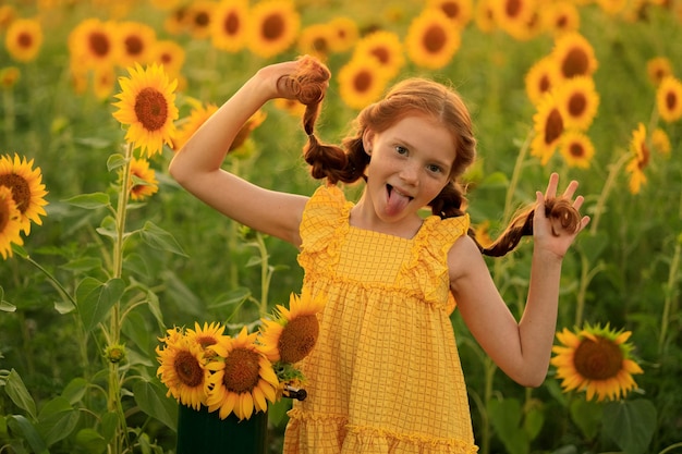Fijne zomer op het platteland, vrolijk roodharig ondeugend meisje met staartjes op een veld met zonnebloemen bij zonsondergang