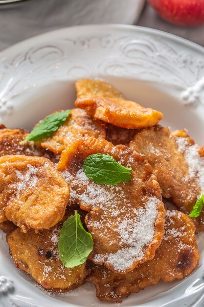 Fijngebakken appelpannenkoekjes bestrooid met vanillesuiker en kaneel gegarneerd met muntblaadjes.