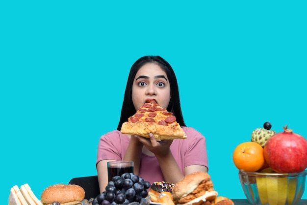 Fijnproever meisje zit aan fruittafel pizza plak te eten met hongerige mond indiaas pakistaans model