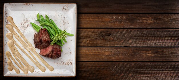 Filet mignon on a white square plate with asparagus and sauce.