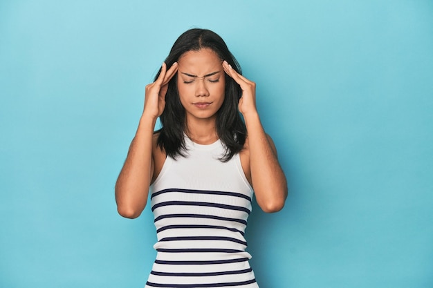 Filipijnse jonge vrouw op blauwe studio die tempels aanraakt en hoofdpijn heeft