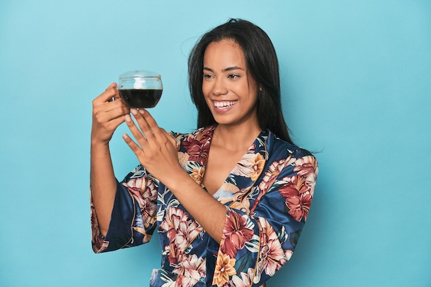 Filipina in floral kimono enjoying a tea moment on blue studio backdrop