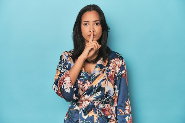 Filipina in bloemenkimono op blauwe studio die een geheim bewaart of om stilte vraagt