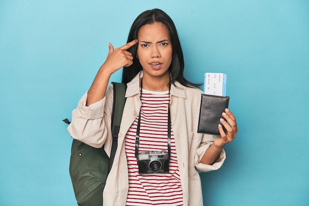 Filipina met camerakaartjes rugzak op blauw met een teleurstellingsgebaar met wijsvinger