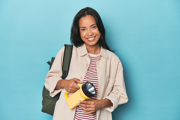 Filipina promoting excursions with lantern and backpack on blue studio