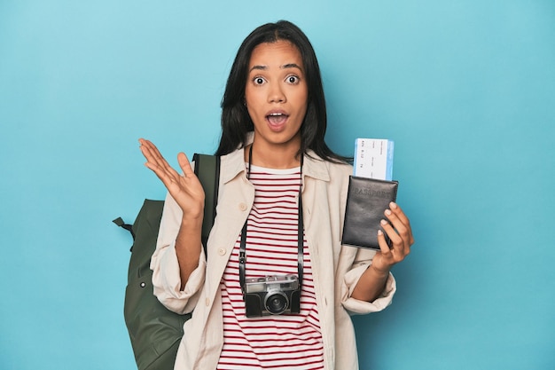 Filipina with camera tickets backpack on blue surprised and shocked