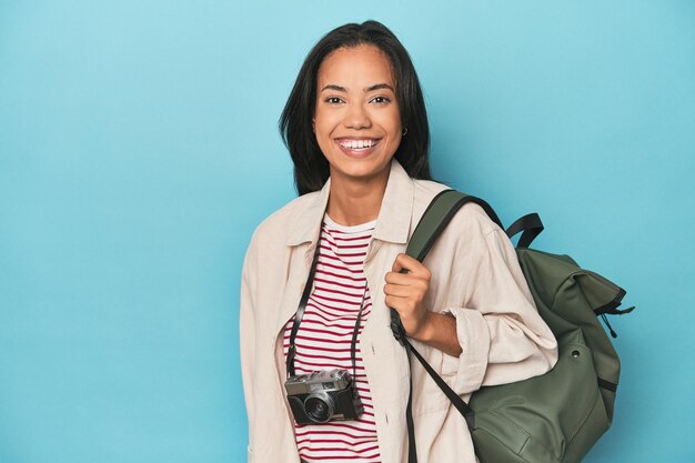 Photo filipina with camera and travel backpack on blue studio backdrop